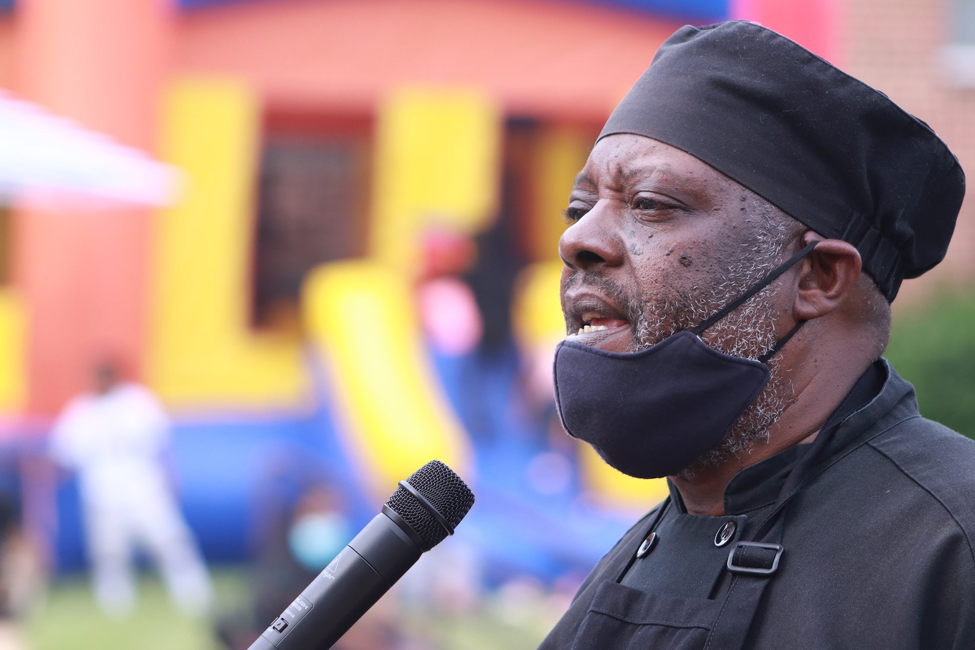 black man with black apron and black chef's hat speaking at a microphone