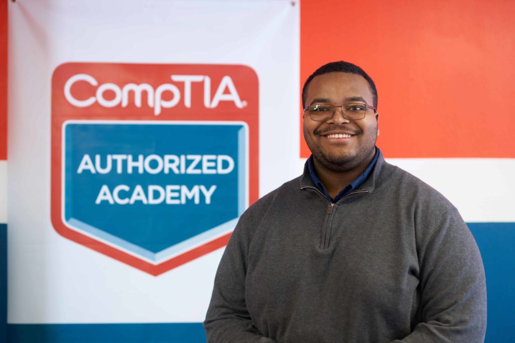 Evan next to a sign that reads "CompTIA Authorized Academy"