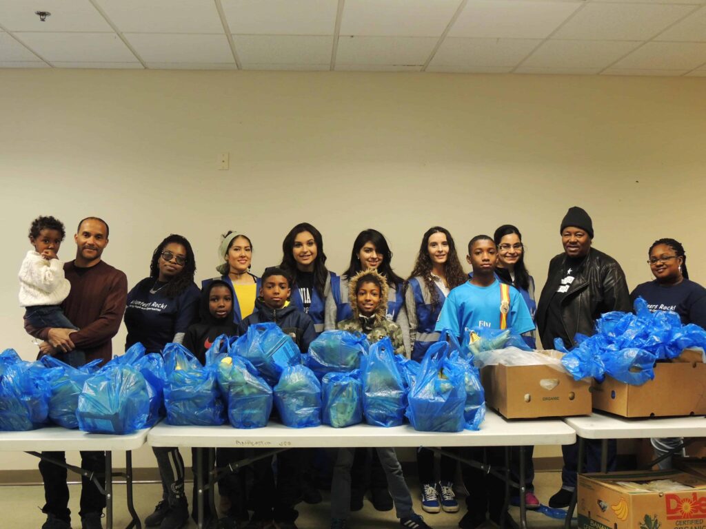 men, women and children of multiple ethnicities posing next to a table full of bags of fresh fruit