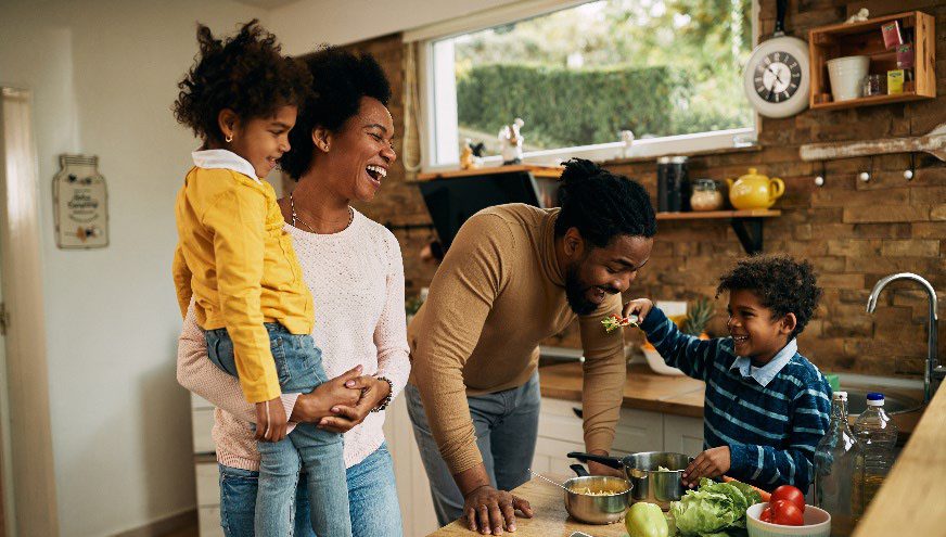 black family with mom, dad and two young kids laughing while making dinner