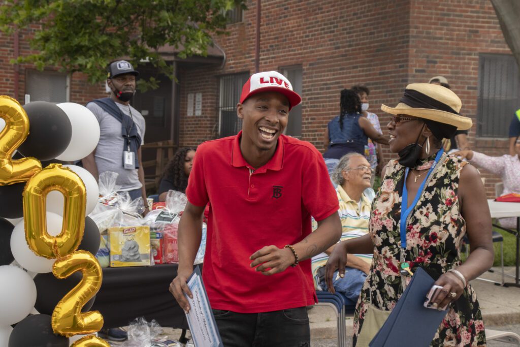 Ms. Shawntay next to a young, black man holding a certificate at an outdoor celebration