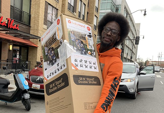 Angelo Brandon carrying a large box with a child double stroller in it