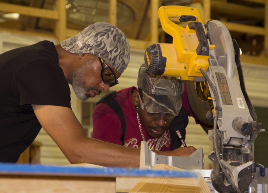 Two construction workers looking at plans in front of a wood cutting machine