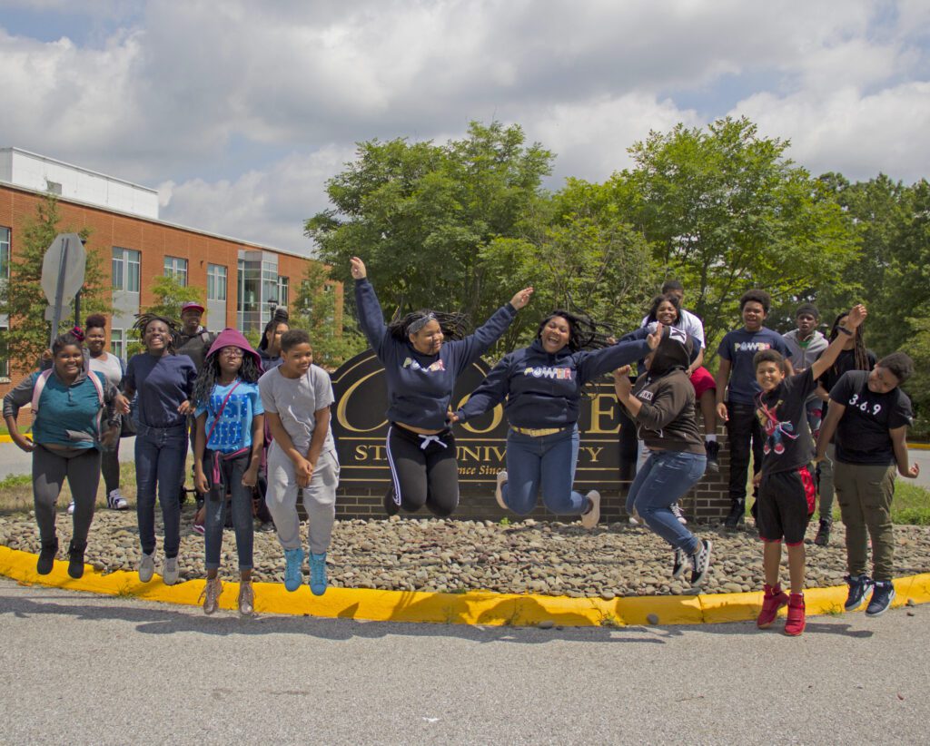 Kids and young adults jumping in front of a university sign