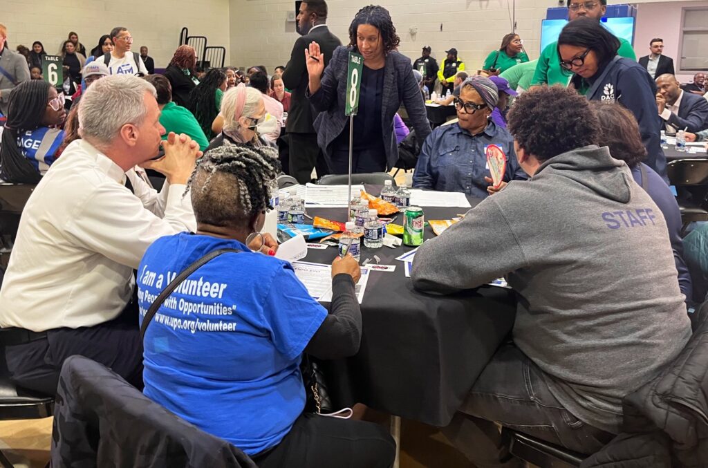 Large community event with people sitting around tables and filling out forms