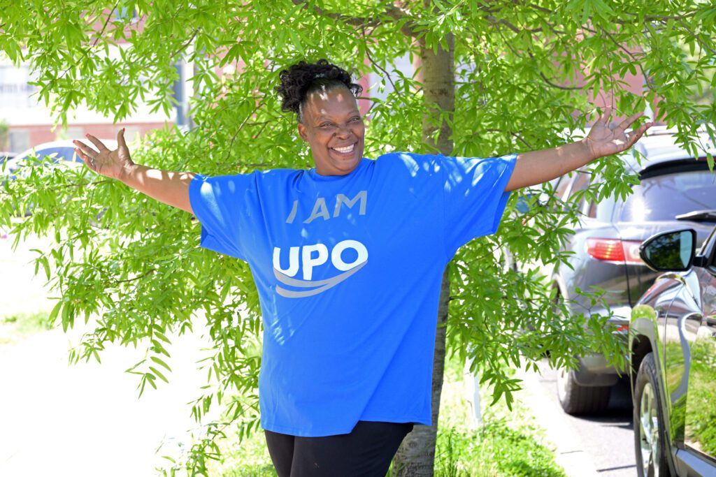 Florence Robinson wearing "I am UPO" shirt, standing in front of a tree with arms outstretched