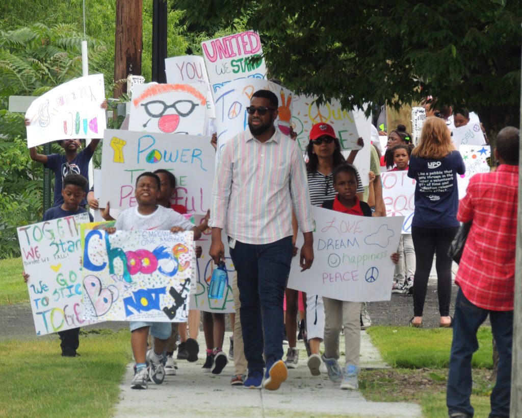 Man leading a group of children holding hand-drawn signs in protest for peace