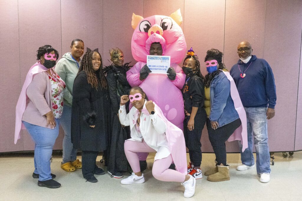 UPO members posing. Some wearing capes and eye-masks like superheroes. At the center is a member wearing an inflatable pig costume, holding a sign saying "We are Covid-19 vaccination site"