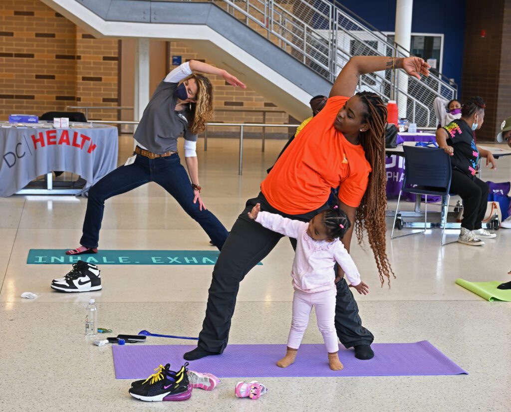 Two women doing yoga, one of them also has their child on the same yoga mat imitating her.