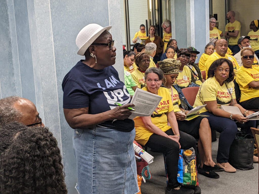 UPO woman standing in a meeting, next to a group of seated attendees