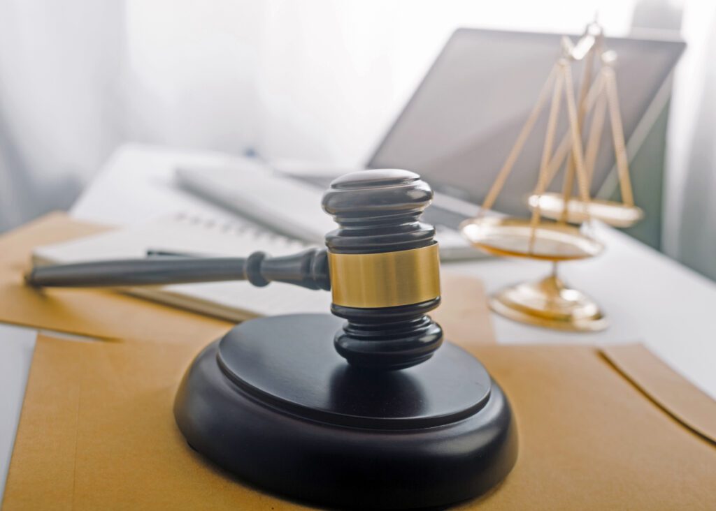 Desk with a gavel in the forefront, behind it are scales and a laptop