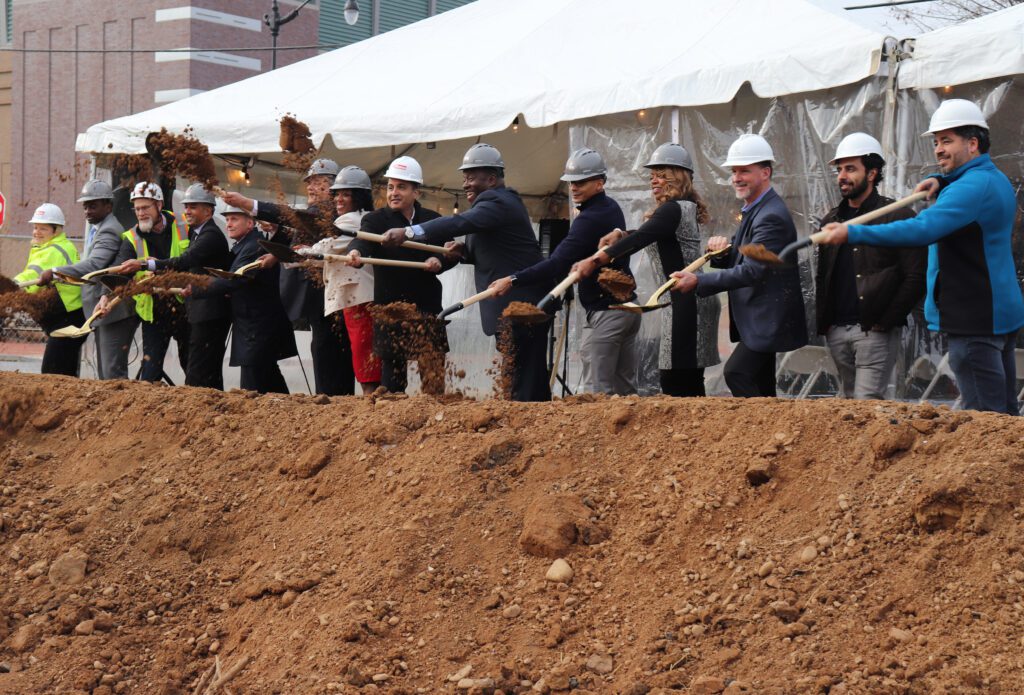 Multiple people ceremoniously flinging dirt into a hole with shovels