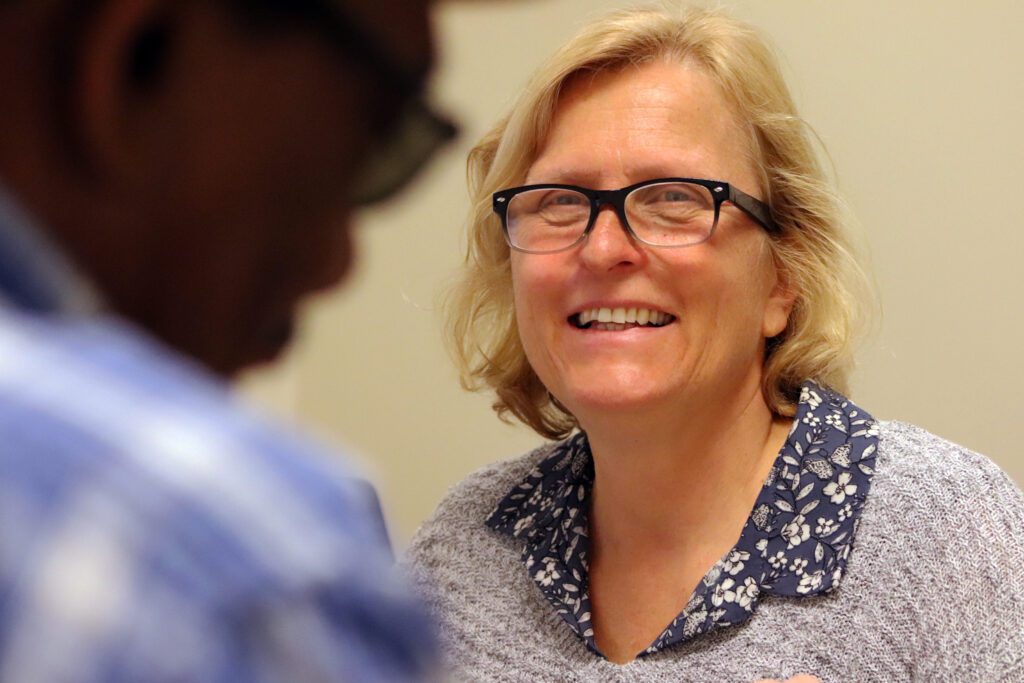 White woman smiling, with the side profile of a black man in the foreground