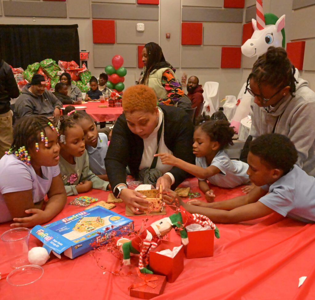 Woman building graham cracker house with children at a Christmas event