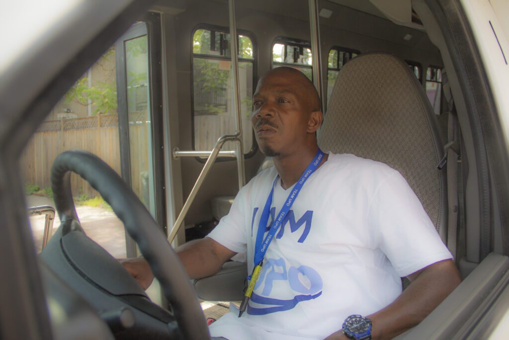 Man wearing "I am UPO" shirt behind the wheel of a bus