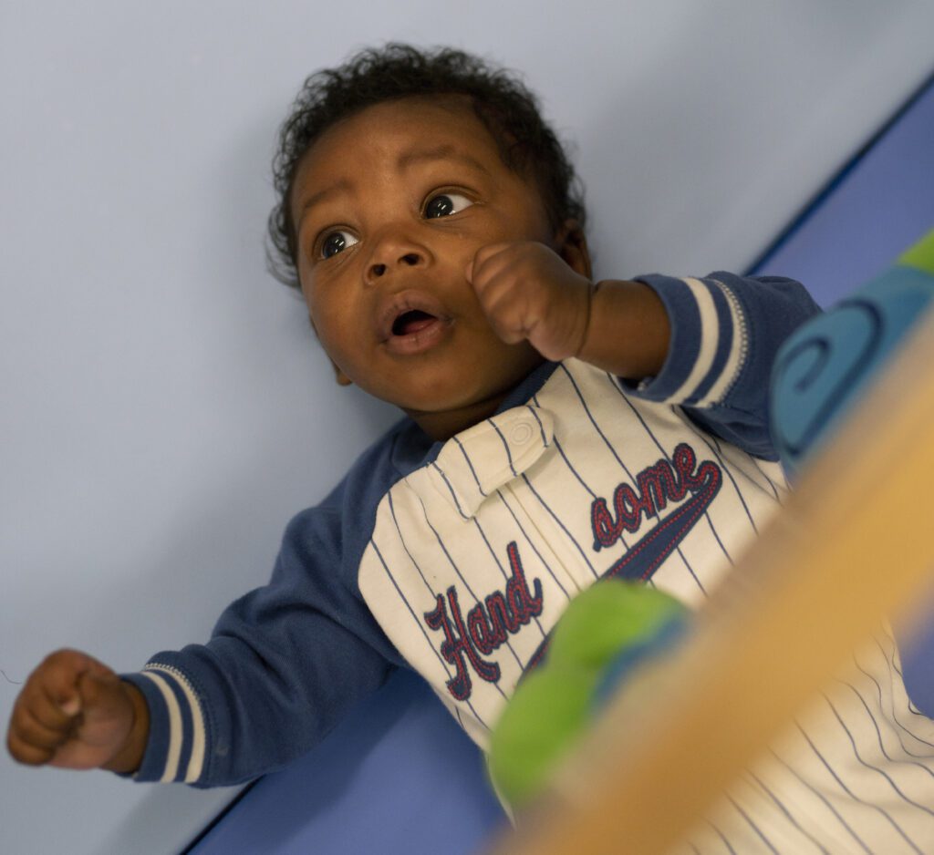 A baby laying down in a baseball jersey style onesie