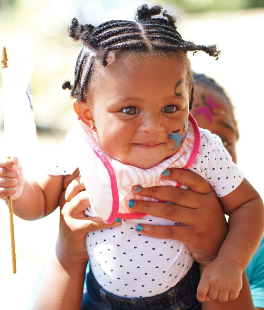 Woman holding up a toddler with face paint